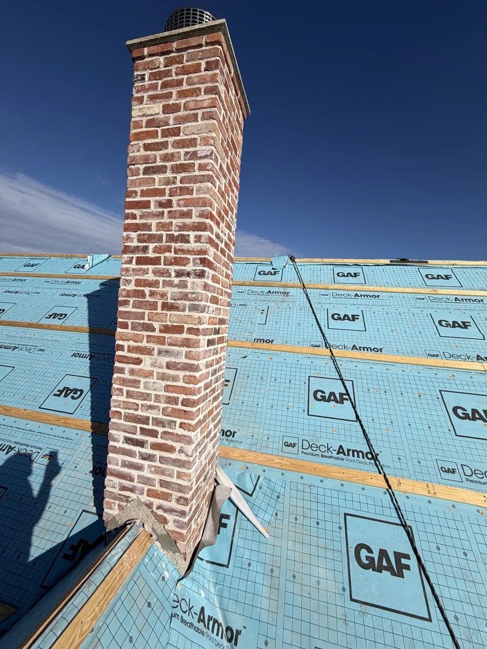 Brick chimney rising past roof battens against a blue sky