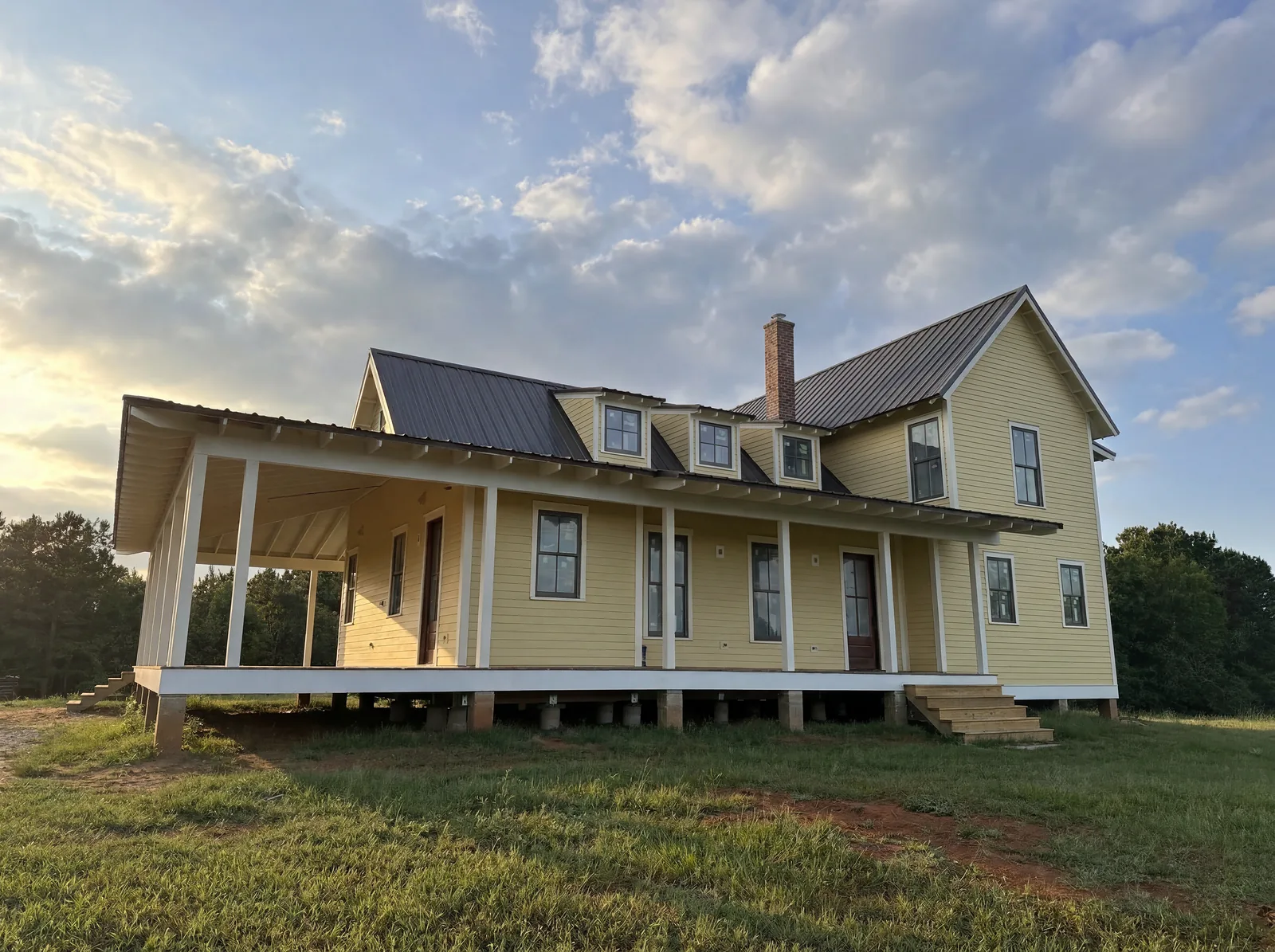 The Caeli House at evening — yellow farmhouse with wraparound porch and dormers
