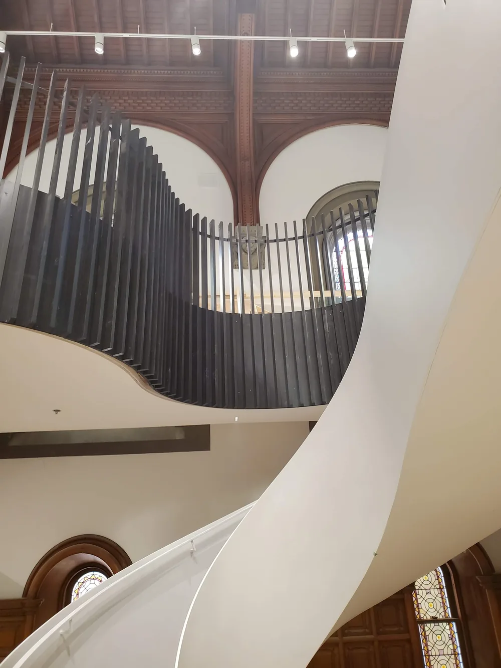Curved wood slat installation beside a historic coffered ceiling and stained glass at the University of Toronto
